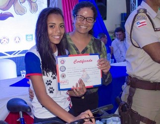 Jovem exibe orgulhosamente o Diploma e a bicicleta que ganhou